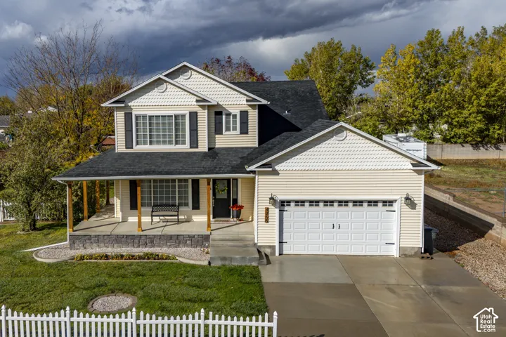 Two-story residence featuring light-colored horizontal siding, dual-pitched roof lines with architectural shingles, covered front porch with timber-style posts, stone-veneer foundation accent, and an attached two-car garage