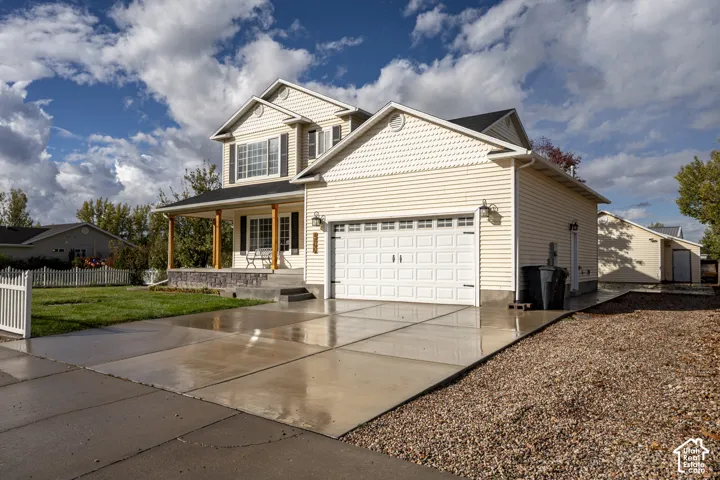 Two-story exterior featuring light-toned horizontal siding, an attached two-car garage, a stone-veneer foundation accent, and a covered front porch with timber-style posts