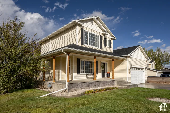 Two-story exterior featuring light-toned horizontal siding, a covered front porch with timber posts, stone-veneer foundation detailing, and an attached two-car garage