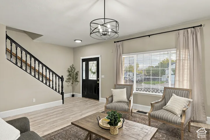 Entryway featuring wood-finish flooring, a matte black metal chandelier, a staircase with a black handrail and balusters, a front door with decorative glass paneling, and a large window with horizontal blinds