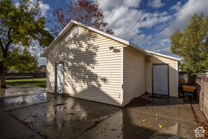 Detached garage structure featuring light-colored horizontal siding, dual entry doors, and an expansive concrete patio