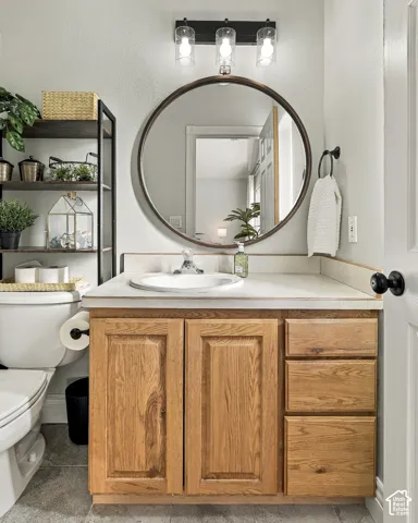 Bathroom vanity featuring natural wood cabinetry, solid surface countertop with integrated sink, circular wall-mounted mirror, three-light fixture with glass shades, and tile flooring