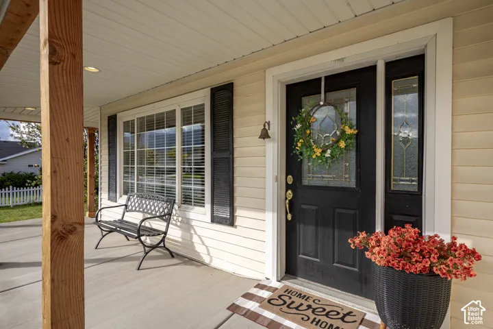 Covered porch featuring wood-finish support posts, exterior siding, a front door with decorative glass inlay and matching sidelight, and multi-paned windows with shutter accents