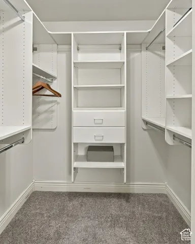 Walk-in closet featuring white built-in shelving, dual soft-close drawers, multiple hanging rods, and neutral carpeting