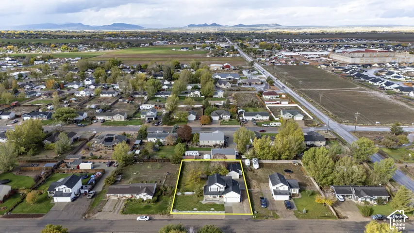 Aerial perspective of a detached residential property featuring a multi-gable roofline, attached multi-car garage, expansive lot with mature trees, and mountainous horizon backdrop
