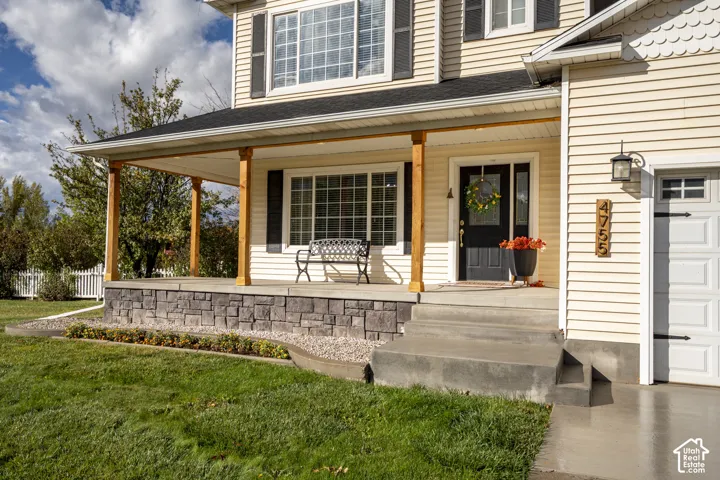 Covered front porch featuring wood support posts, stone-veneer foundation, concrete steps, and a multi-lite front door with sidelight