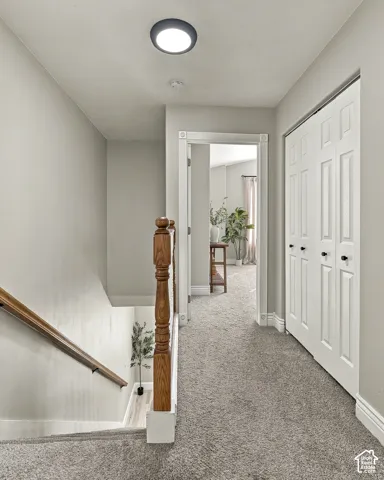 Hallway featuring wall-to-wall carpeting, wood-finish stair railing with matching balusters, and a floor-to-ceiling bi-fold closet with matte black hardware