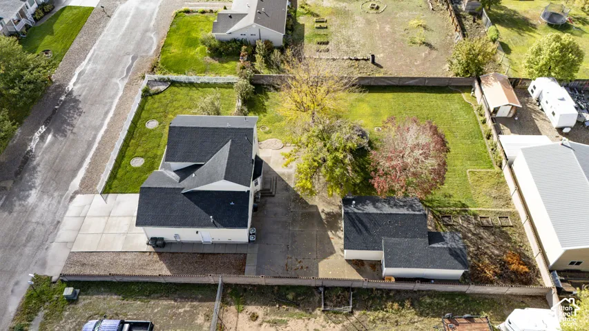 Aerial perspective of property featuring a detached garage, concrete driveway, fenced yard, and established trees