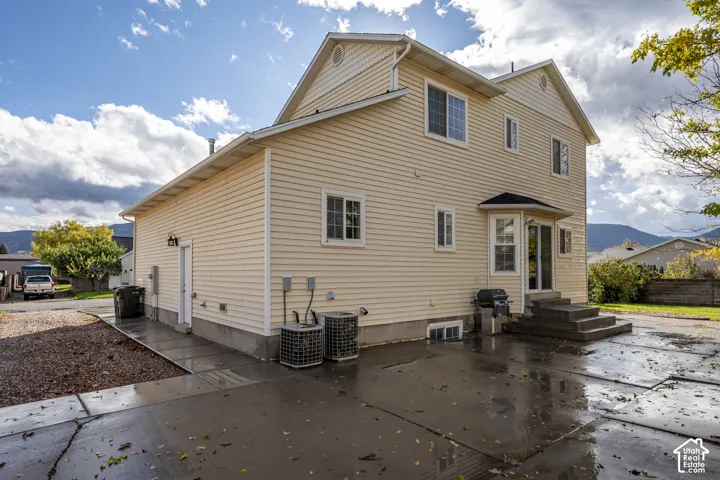 Two-story vinyl-sided exterior featuring a concrete patio, exterior access door, and mountain backdrop