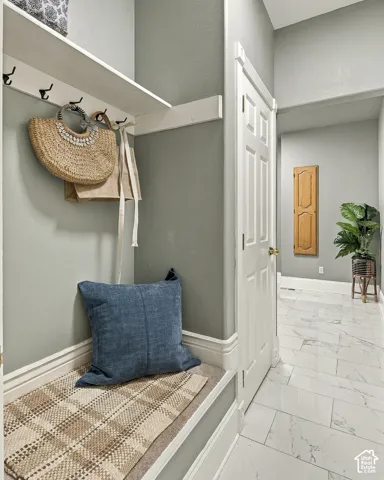 Built-in bench with overhead shelf and wall-mounted hooks, white paneled interior door, and light-toned stone-finish tile flooring
