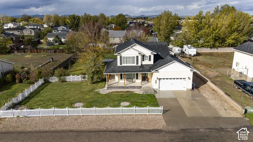 Two-story residence featuring a covered front porch, attached garage, white vinyl perimeter fencing, and concrete driveway