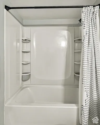Full-size bathtub featuring a white acrylic surround with integrated shelving units and a matte black shower rod