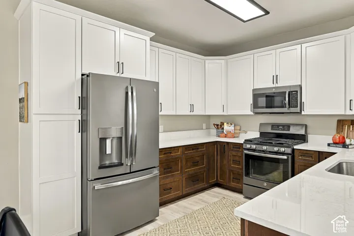 Kitchen featuring two-tone cabinetry with white upper and dark wood lower cupboards, white countertops, stainless steel appliances, and flush-mount overhead lighting