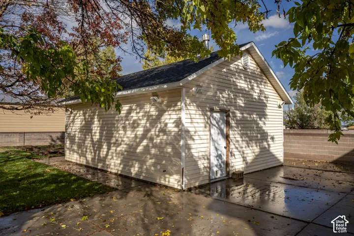 Detached structure featuring light-colored horizontal siding, a gabled roof with dark shingles, a single exterior door, and a concrete pad surround