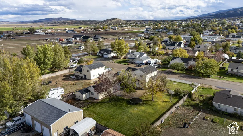 Aerial perspective of a detached residential property featuring an expansive lawn, mature trees, a detached three-car garage with metal roofing, and perimeter fencing