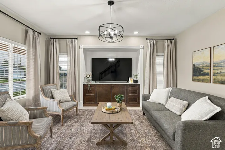 Custom built-in cabinetry featuring wood-finish lower storage, recessed lighting, matte black geometric chandelier, and multiple windows with wide-slat blinds