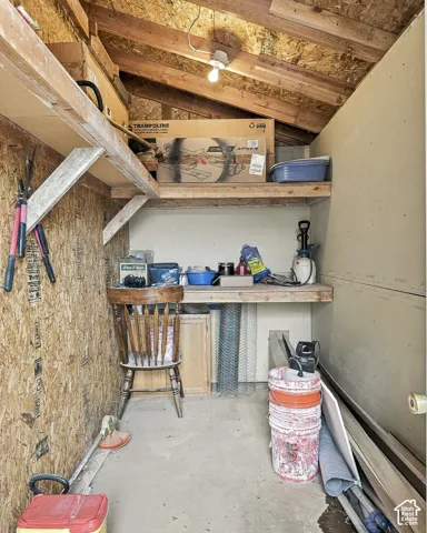 Storage area featuring exposed timber rafters, oriented strand board wall construction, fixed timber shelving, and a built-in wooden workspace surface