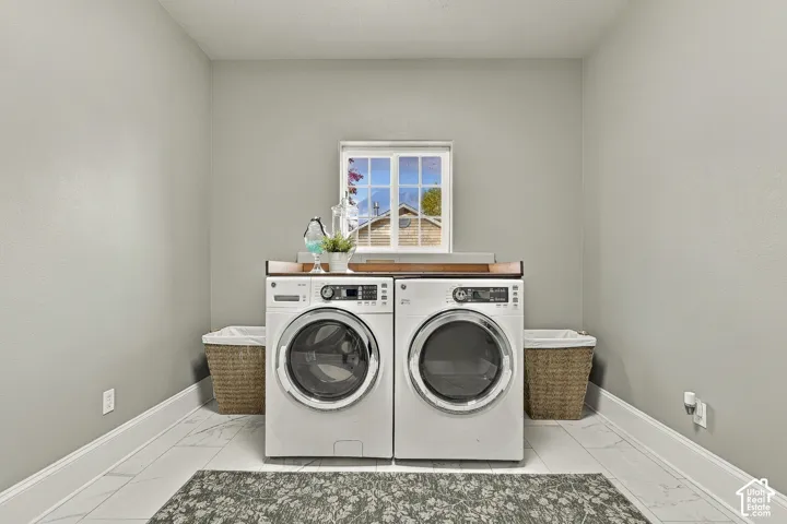Dedicated laundry room featuring large-format stone-style tile flooring, white wall finish, and a wood-topped folding counter