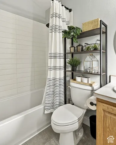 Full-height light-toned wall tile surrounding the bathtub, neutral tile flooring, and light oak-finish cabinetry with a solid-surface countertop