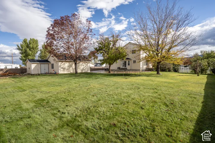 Expansive backyard featuring a large grass lawn, mature trees, a detached storage building, and perimeter fencing