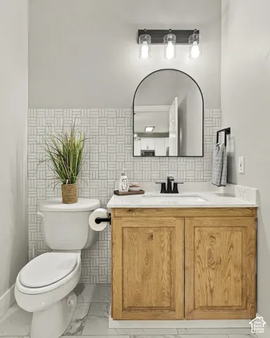 Bathroom featuring a wood-finish vanity with a stone-surface countertop, an arched-top mirror, decorative basketweave-pattern wall tile, and matte black fixtures