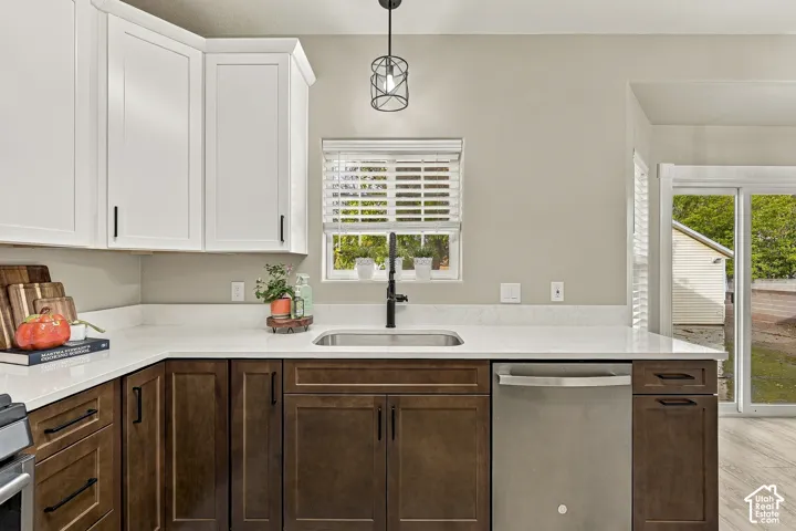 Two-tone cabinetry featuring white upper and dark wood-finish lower cabinets, stone countertops, stainless steel dishwasher, matte black hardware, and an industrial-style pendant light fixture