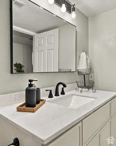 Vanity featuring a stone-surface countertop, an integrated rectangular sink, a black-framed wall mirror, matte black faucet hardware, and a three-bulb vanity light fixture