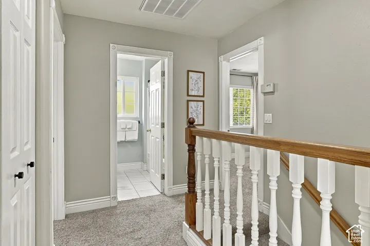 Neutral-toned interior featuring a staircase with white balusters and a natural wood-finish handrail, multi-panel doors with matte black hardware, and crisp door casing with decorative corner blocks