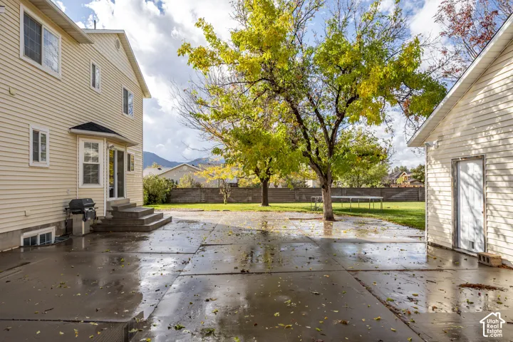 Large concrete patio with vinyl siding, mature trees, lawn, and perimeter fencing