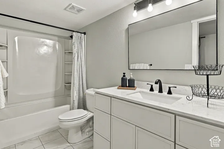 Bathroom featuring a white vanity with a light stone-finish countertop, undermount sink, matte black widespread faucet, expansive framed wall mirror, and a tub-shower combination with built-in shelving