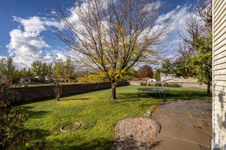 Backyard featuring a concrete patio, stone-bordered landscape bed, grass lawn, mature trees, and perimeter masonry fencing