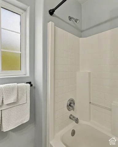 Bathtub and shower surround featuring white square wall tile, privacy-glass window, matte black shower rod, and chrome plumbing fixtures