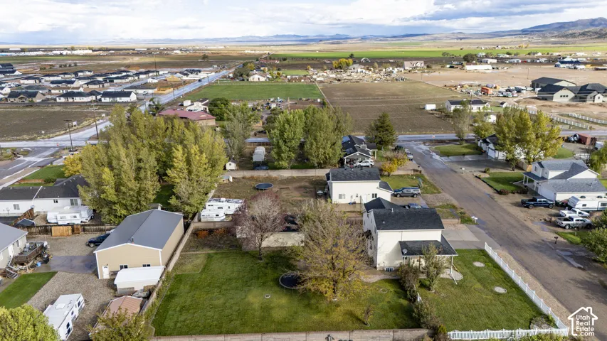 Aerial perspective of a property featuring a multi-story residence, a detached garage with a metal roof, expansive lawn space, mature deciduous trees, and a perimeter fence
