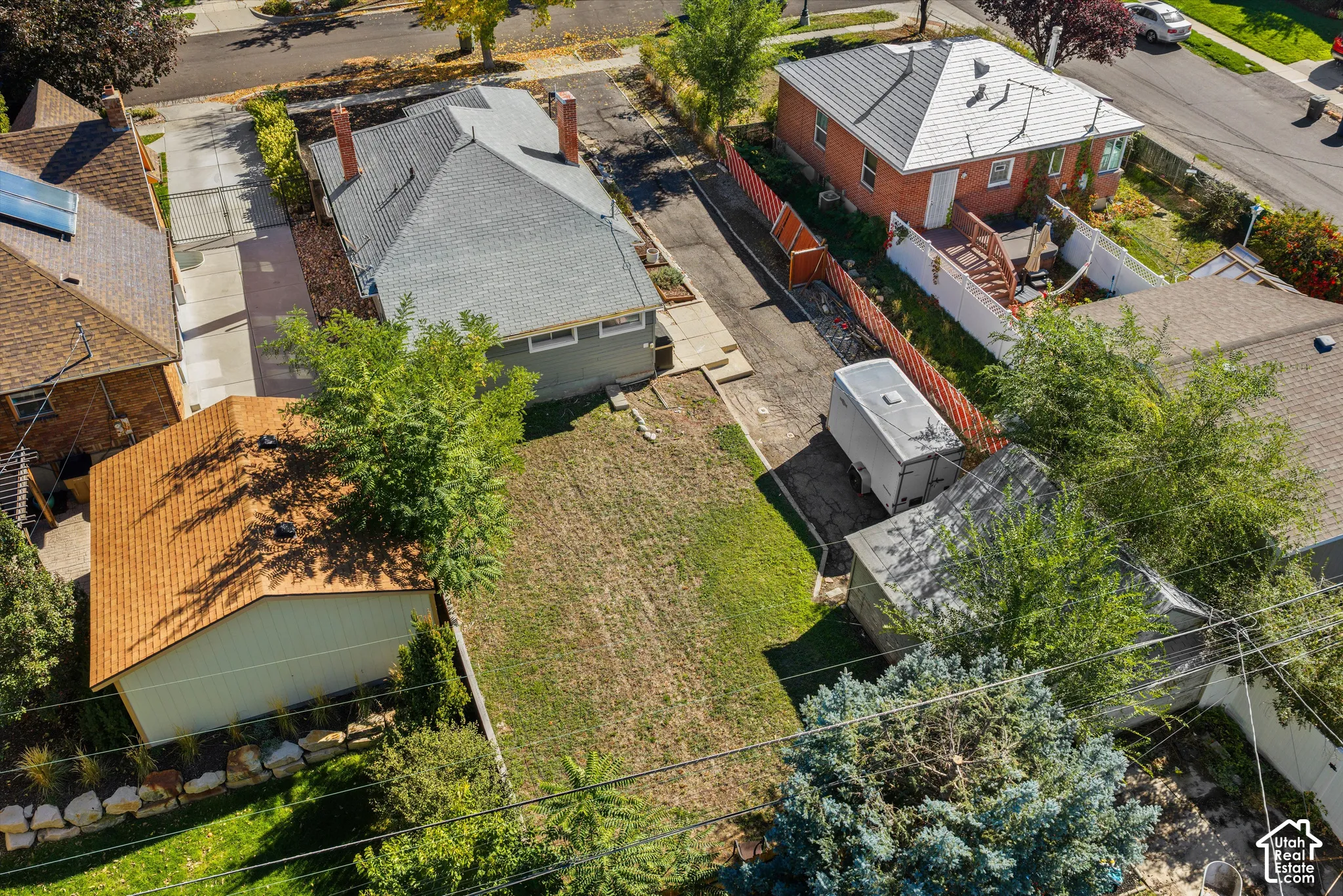Aerial perspective of a detached residential property featuring a dedicated asphalt driveway, a detached storage structure, and a fenced rear yard with mature trees