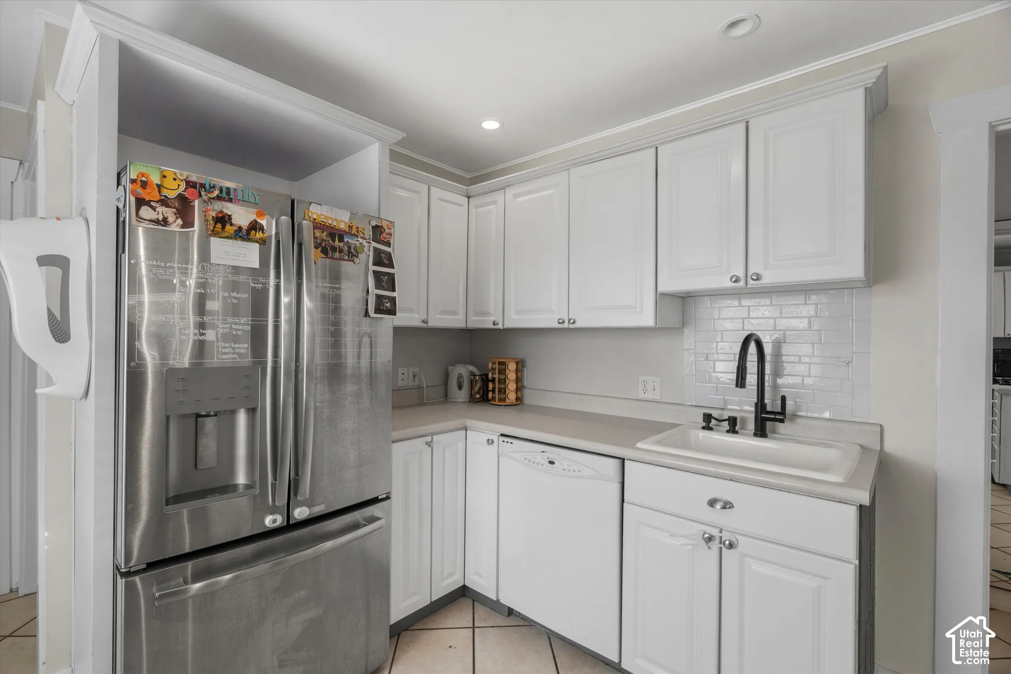 Kitchen featuring white cabinetry, subway tile backsplash, stainless steel refrigerator, undermount sink with a matte black faucet, and dishwasher