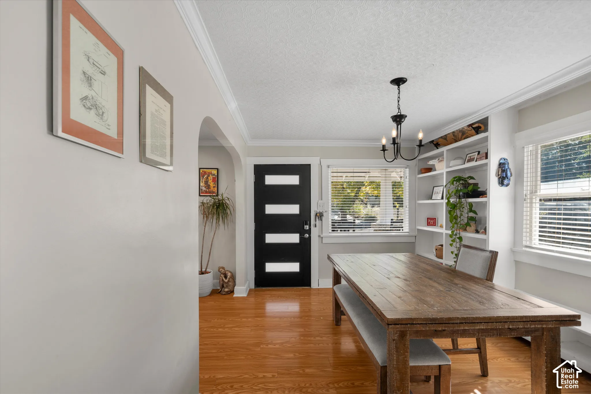 Polished wood-finish flooring, built-in floor-to-ceiling white shelving, arched architectural entry, modern black four-panel front door with horizontal frosted glass insets, and a classic multi-arm chandelier