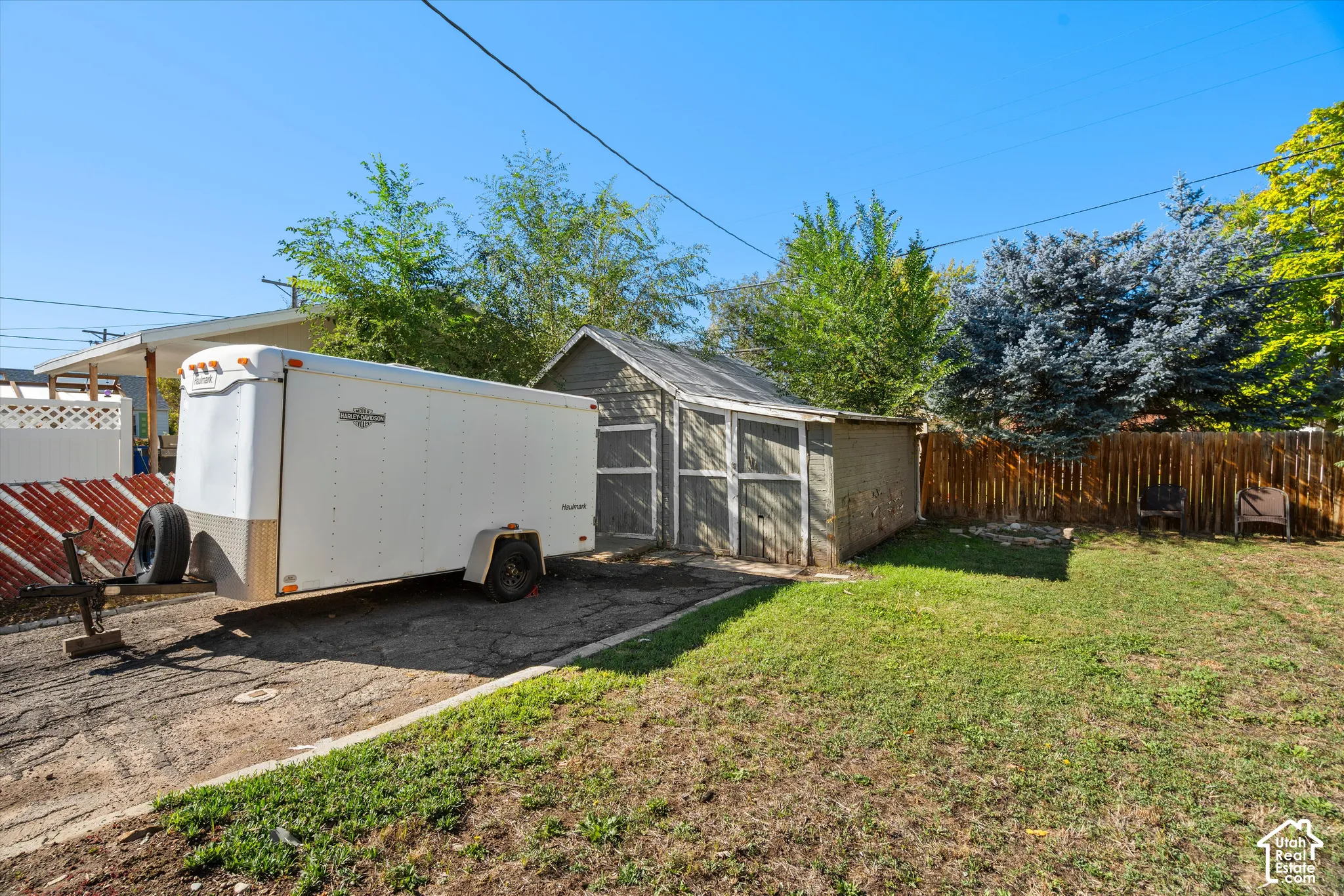 Detached storage structure with dual access doors, asphalt surfacing, and wooden privacy fencing