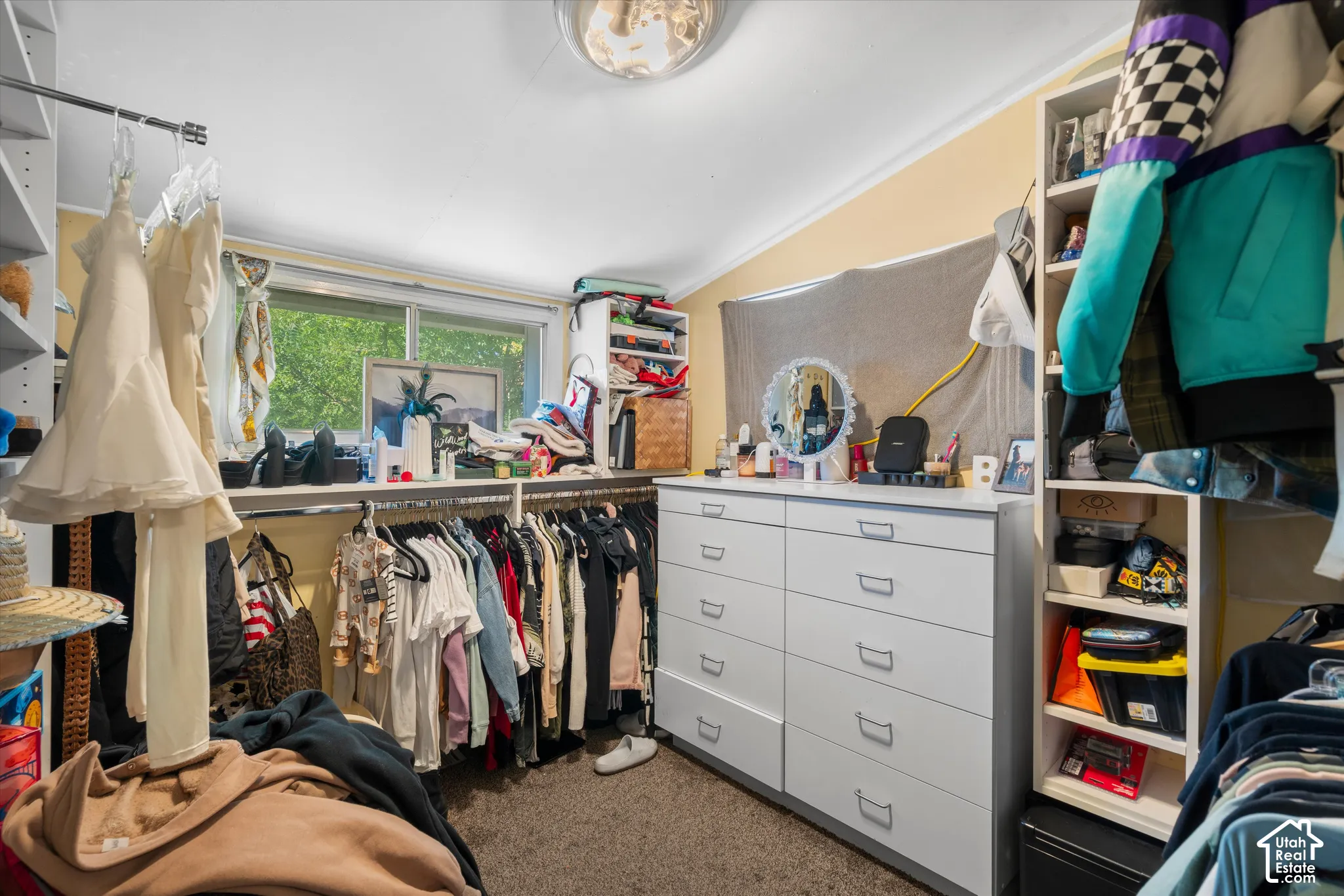 Storage room featuring wall-to-wall built-in shelving, integrated closet rod systems, a multi-drawer dresser, and a sliding window