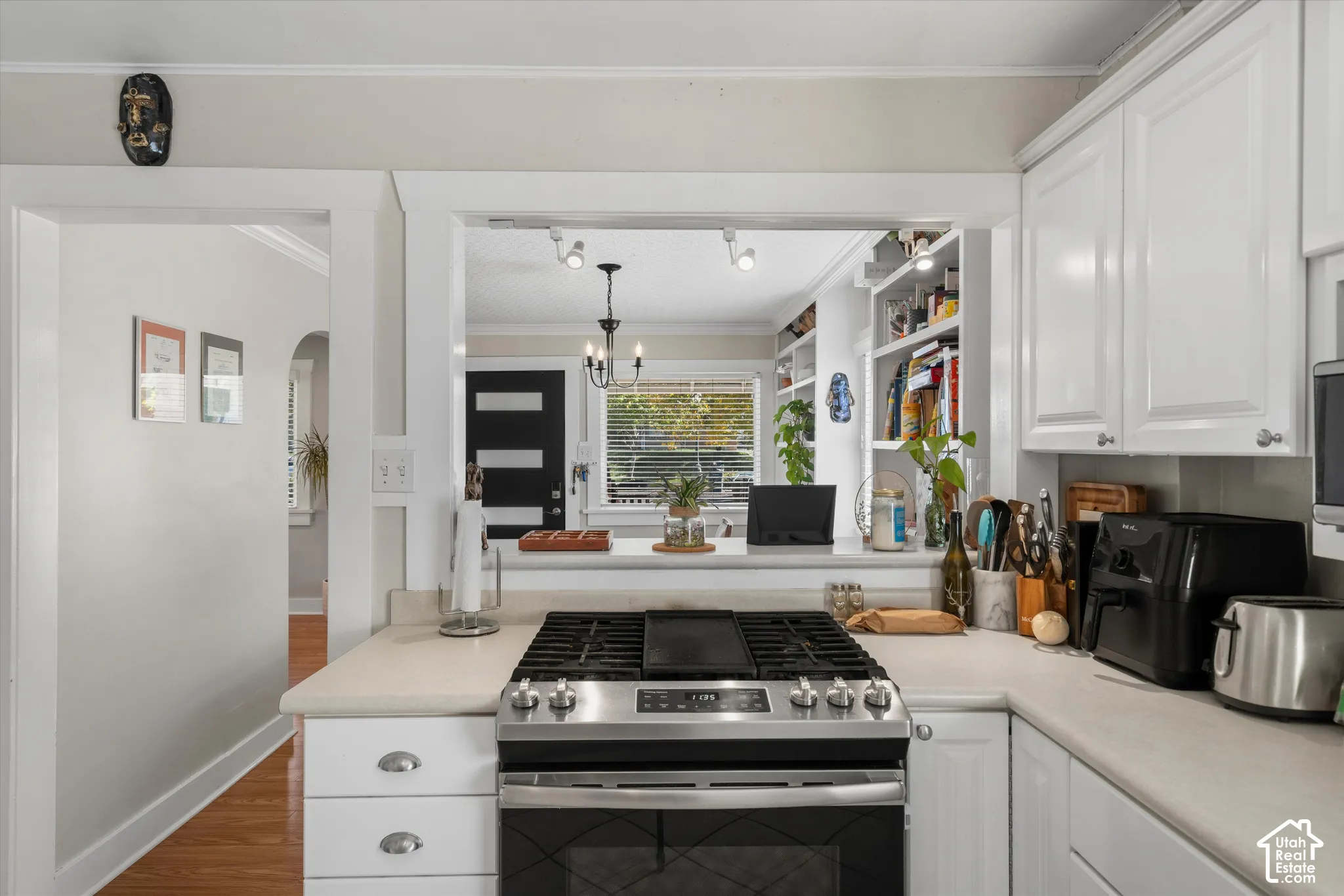 Kitchen featuring white shaker-style cabinetry, light-toned countertops, a stainless steel gas range with a center griddle, and built-in white shelving