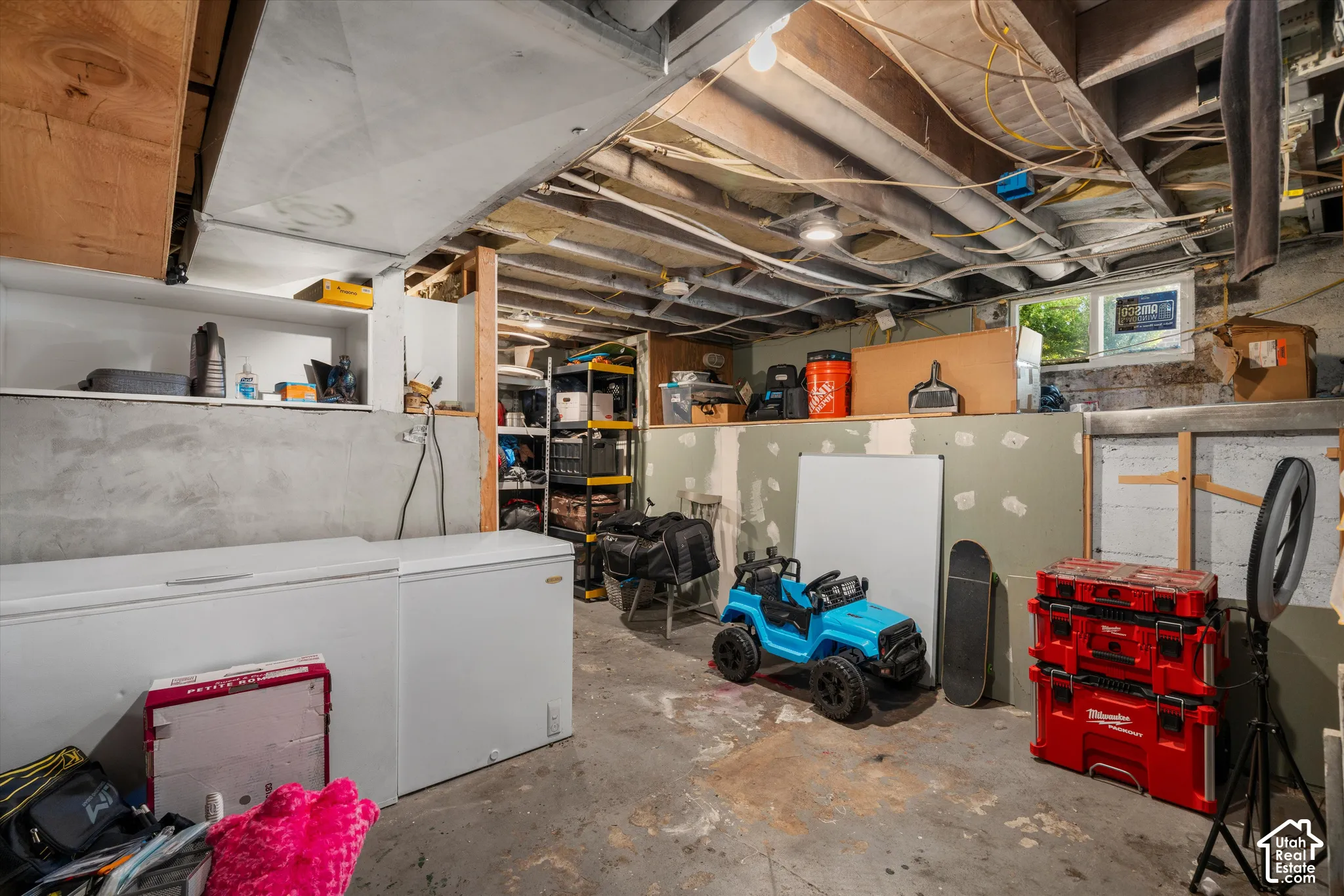 Unfinished storage space featuring exposed ceiling joists, concrete flooring, concrete foundation walls, and an exterior egress window