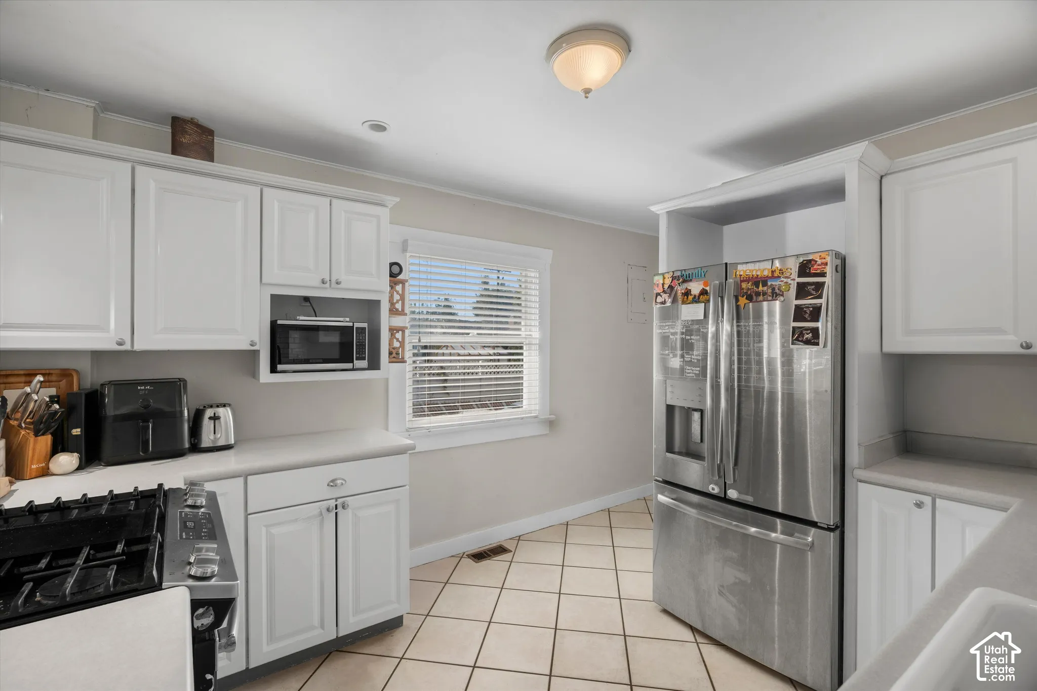 Kitchen featuring white shaker-style cabinetry, stainless steel refrigerator, gas range, tile flooring, and integrated microwave nook