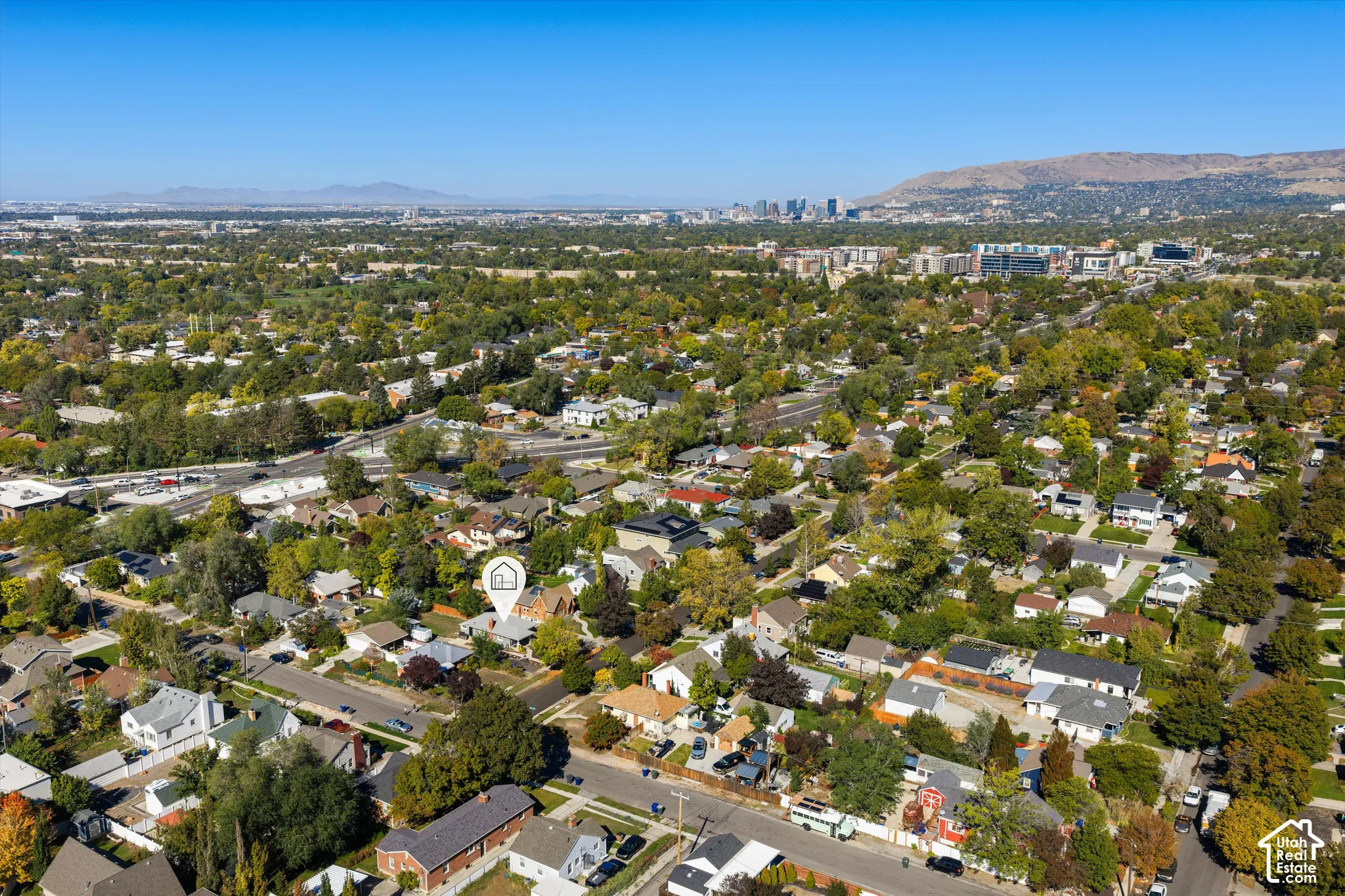 Aerial perspective of residential property featuring mature trees, expansive neighborhood foliage, and mountain backdrop