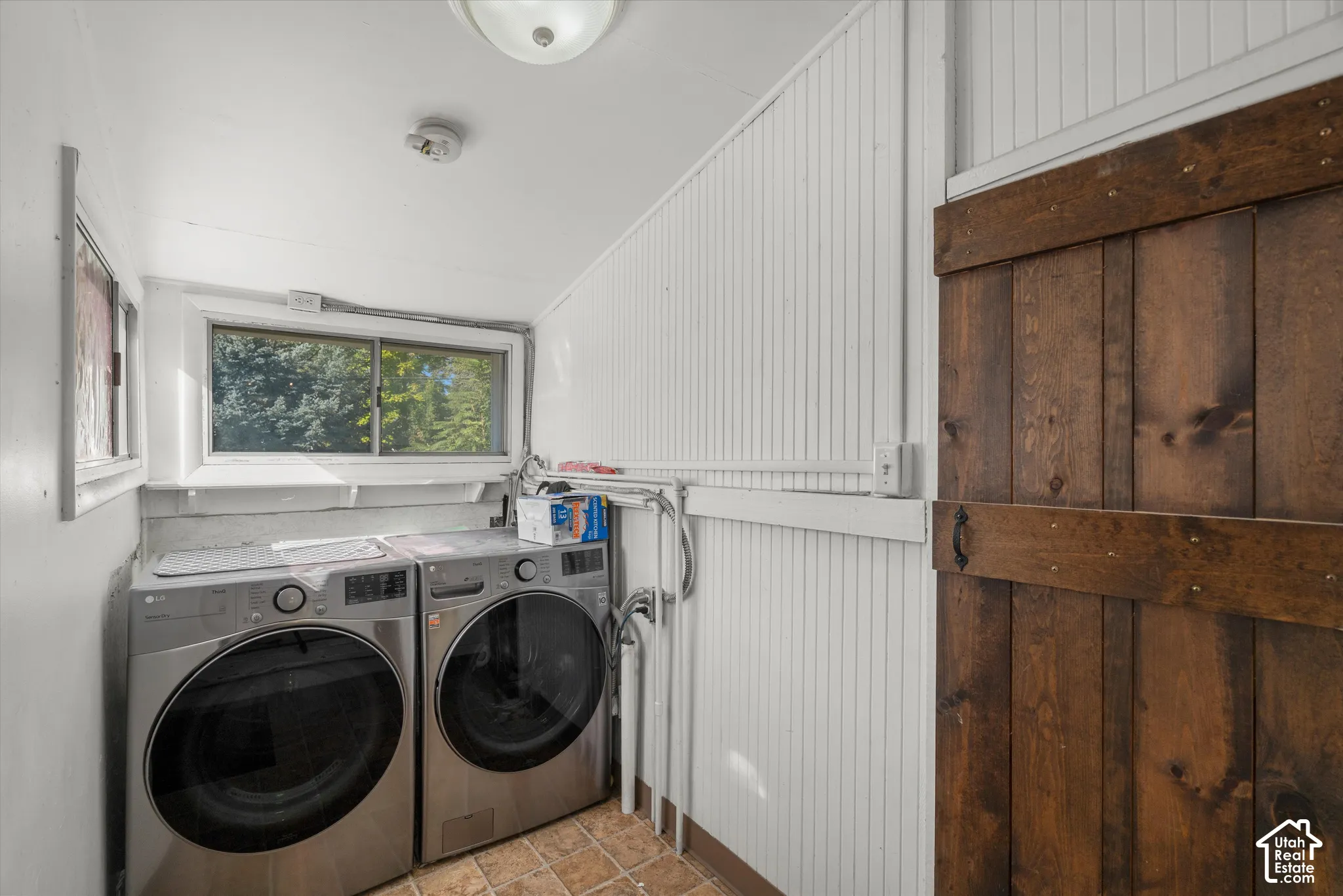 Utility space featuring white vertical beadboard wall paneling, tile flooring, and a sliding dark-stained wood barn door