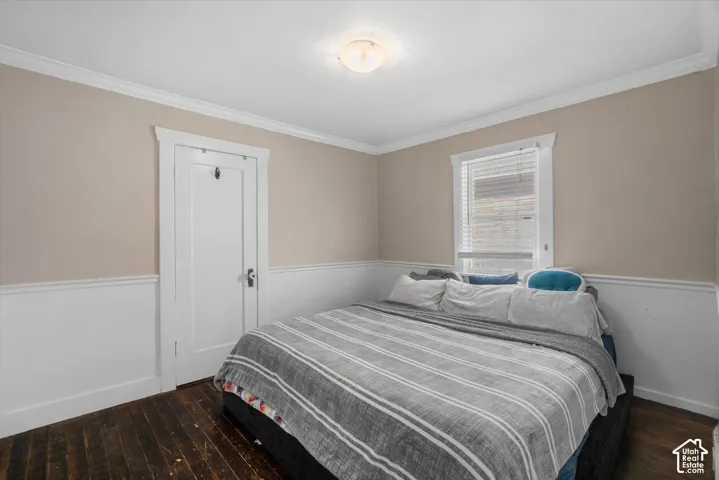 Room featuring wood flooring, white wainscoting, crown molding, and a paneled interior door with trim