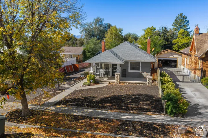 Exterior featuring a gray-sided bungalow with dual brick chimneys, stone-columned front porch, paved driveway, and detached garage