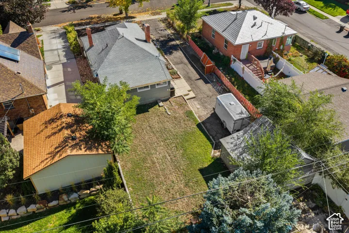 Aerial perspective of a detached residential property featuring a dedicated asphalt driveway, a detached storage structure, and a fenced rear yard with mature trees