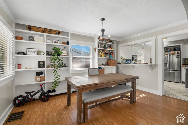 Dining area featuring wood-finish flooring, extensive built-in white shelving, crown molding, a decorative chandelier, and a pass-through window with a shelf