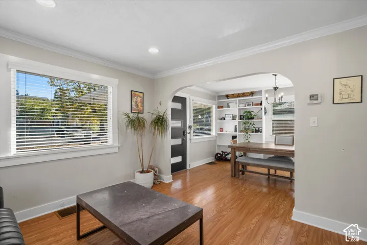 Living area featuring wood-finish flooring, an arched entryway, recessed lighting, crown molding, and built-in shelving