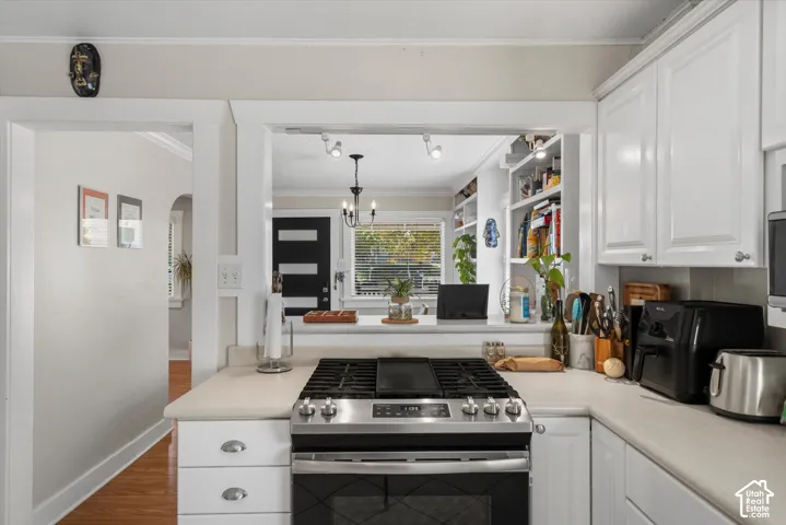 Kitchen featuring white shaker-style cabinetry, light-toned countertops, a stainless steel gas range with a center griddle, and built-in white shelving