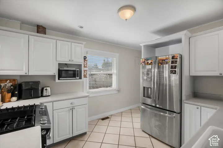 Kitchen featuring white shaker-style cabinetry, stainless steel refrigerator, gas range, tile flooring, and integrated microwave nook